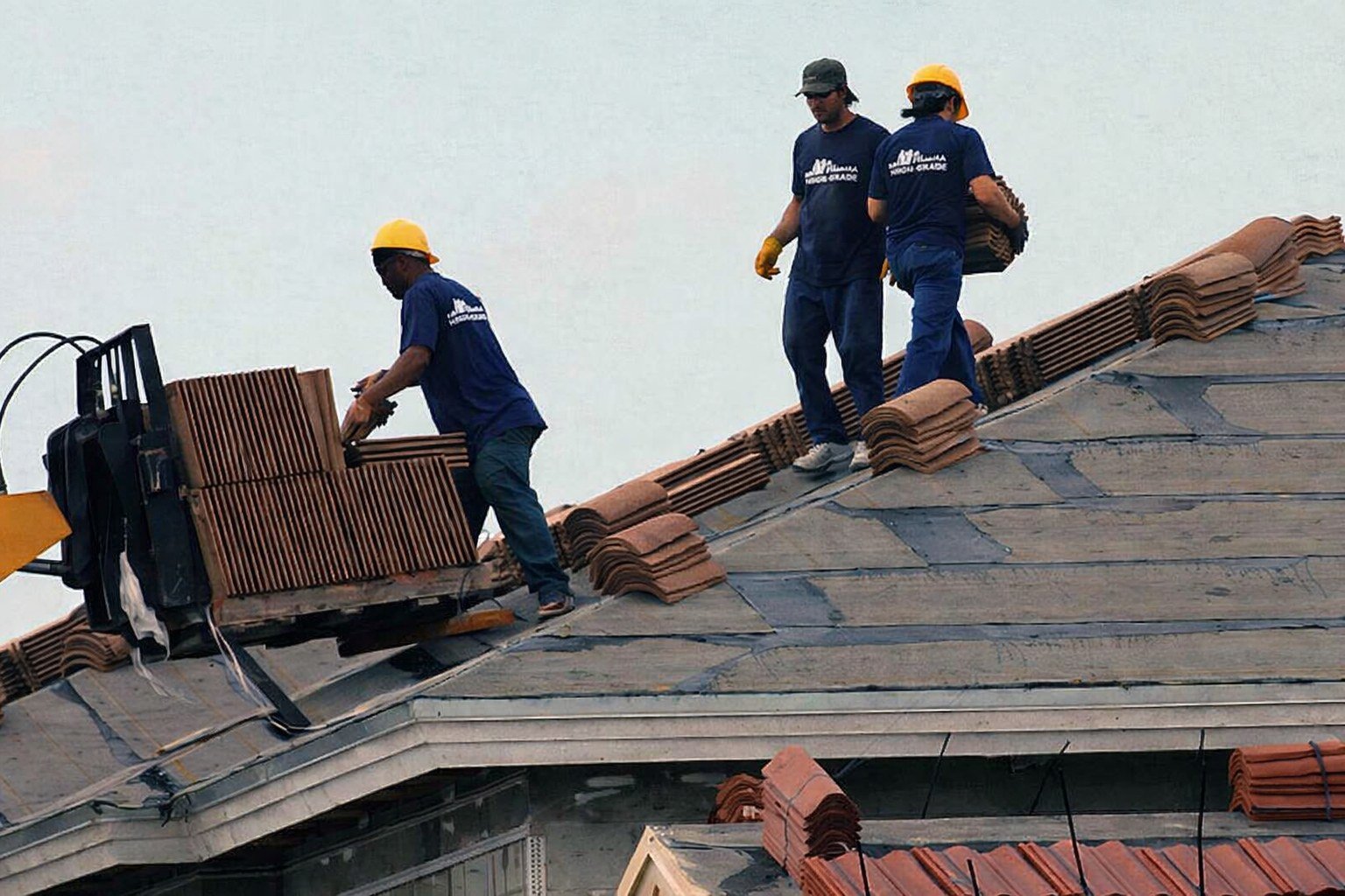 Roofers installing terracotta tiles on sloped roof